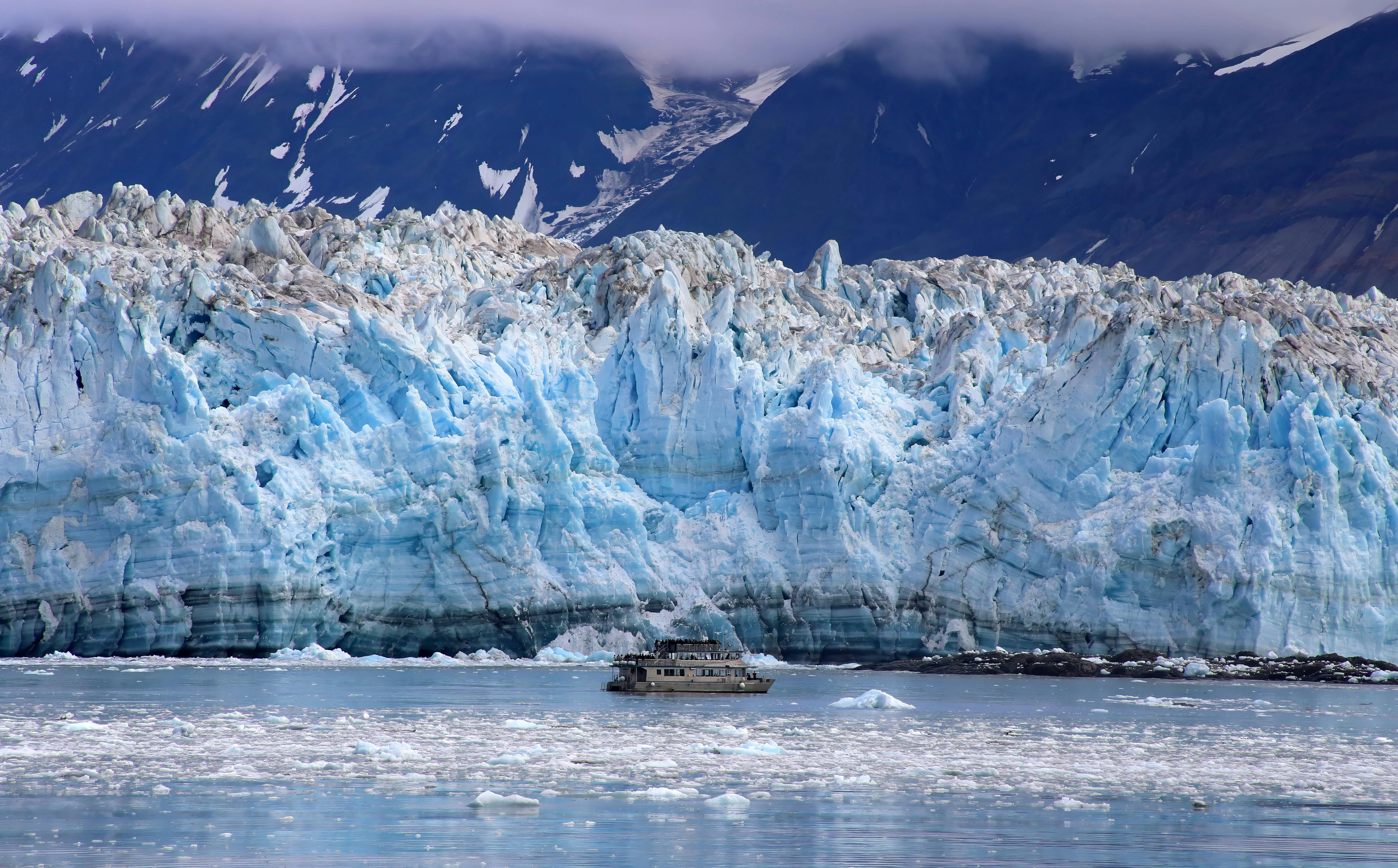 A small cruise ship drifts near the towering blue ice of Hubbard Glacier
