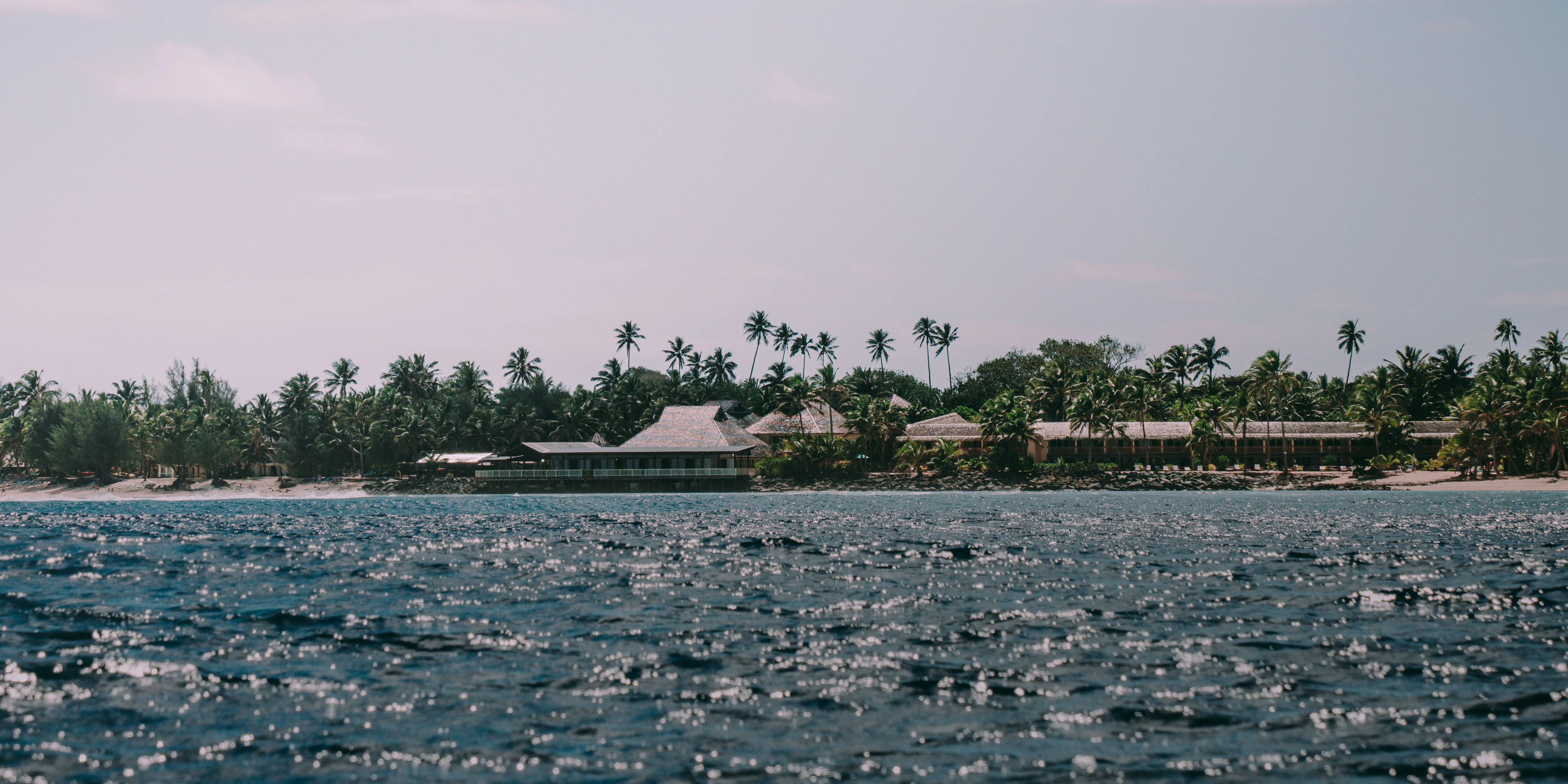 A tranquil beachfront resort, featuring tropical villas nestled among swaying palm trees beside a pristine white-sand beach 