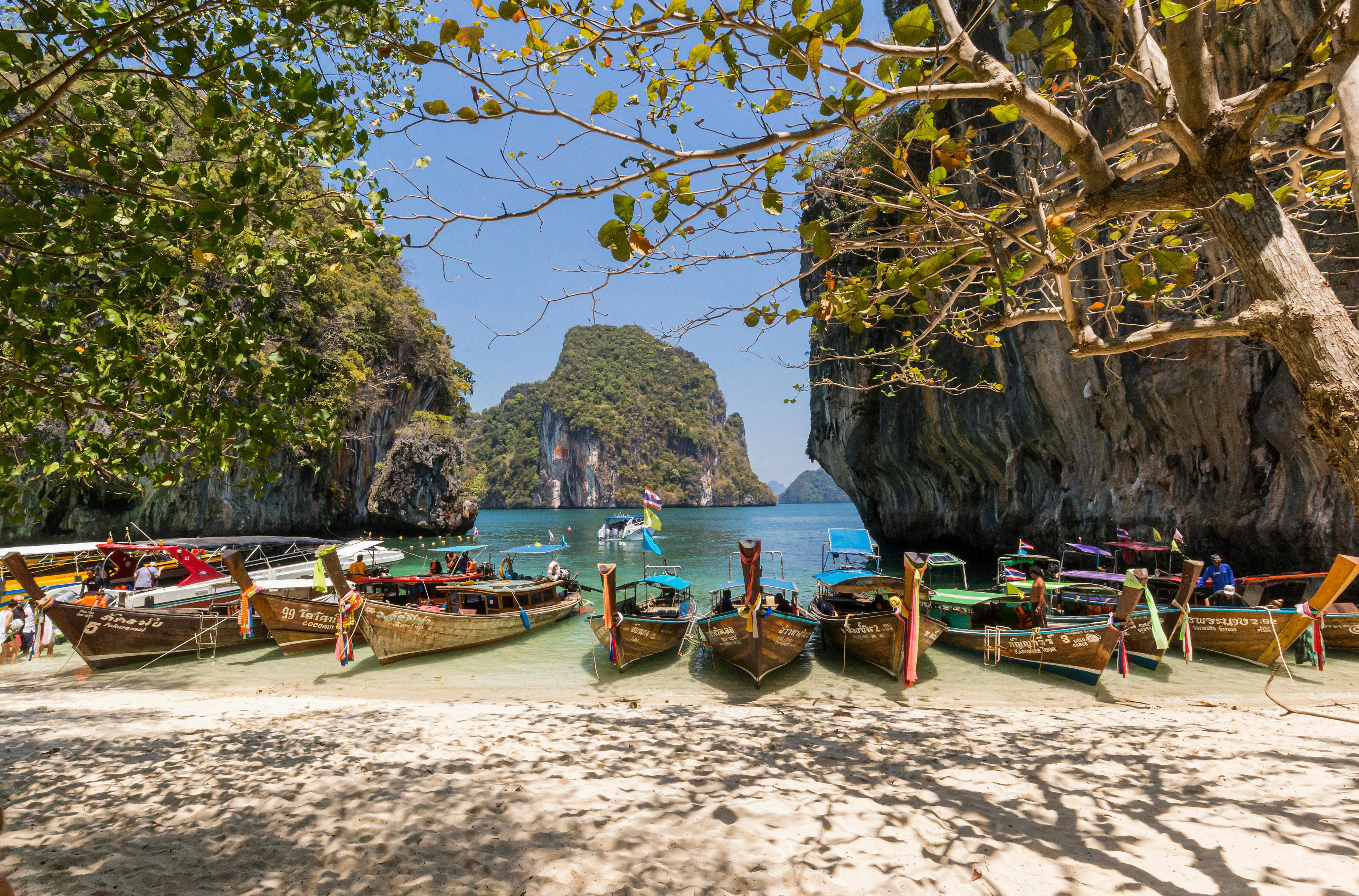 Traditional long-tail boats rest along a golden beach in southern Thailand