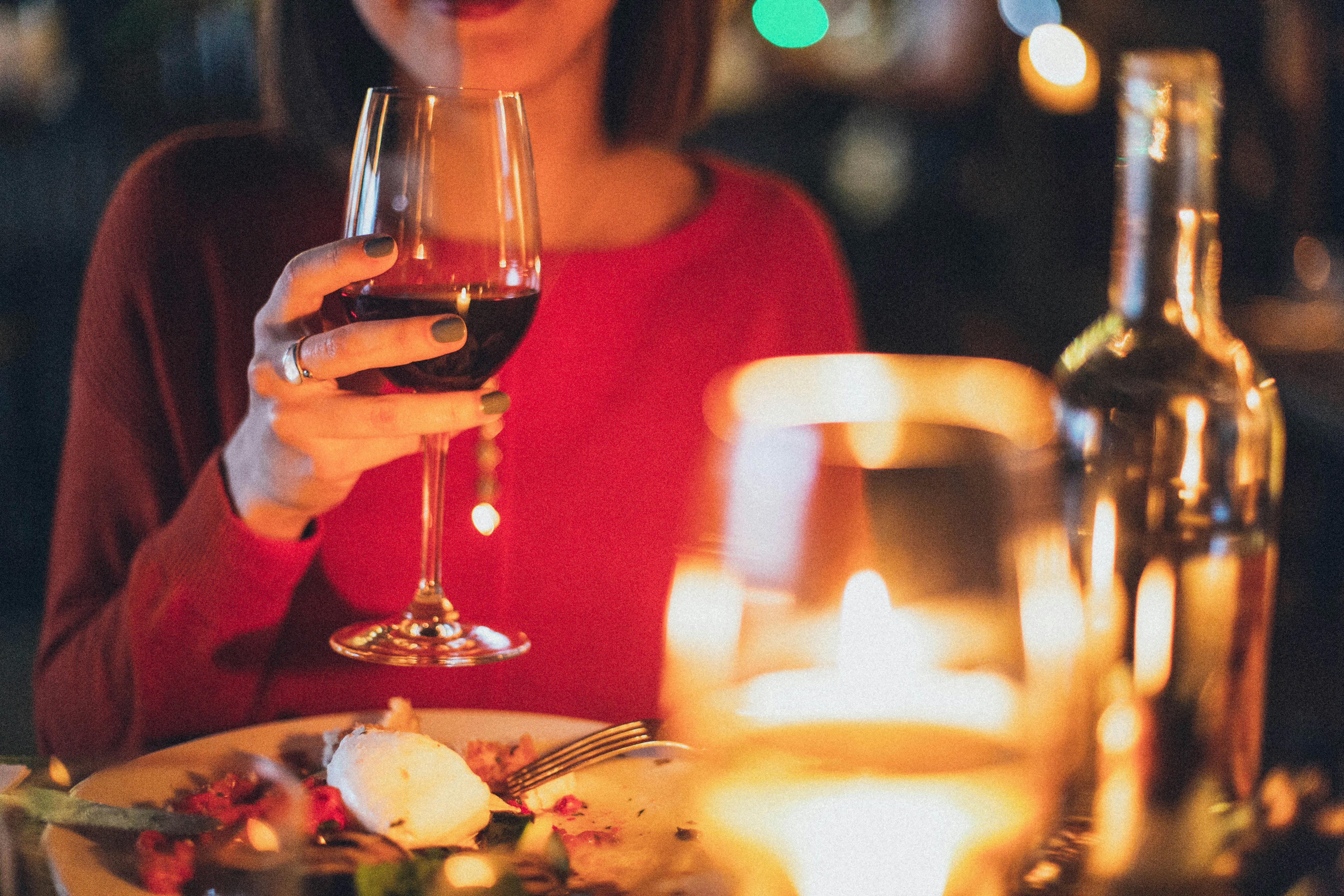 A woman in a red top holding a glass of red wine during a luxurious candlelit dinner at a restaurant